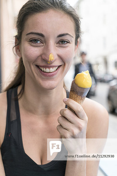 Porträt einer lächelnden jungen Frau mit Eistüte und Eiscreme an der Nase