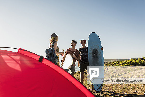 Drei Freunde mit Surfbrettern beim Camping am Meer