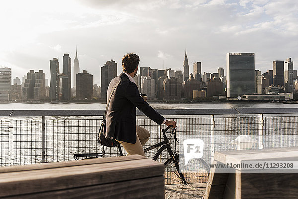 USA  New York City  Geschäftsmann auf dem Fahrrad mit Blick auf die Skyline von Manhattan