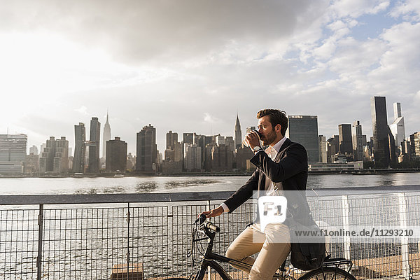 USA  New York City  Geschäftsmann auf dem Fahrrad mit Kaffee zum Mitnehmen