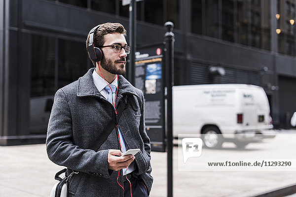 USA  New York City  Geschäftsmann mit Handy und Kopfhörer unterwegs
