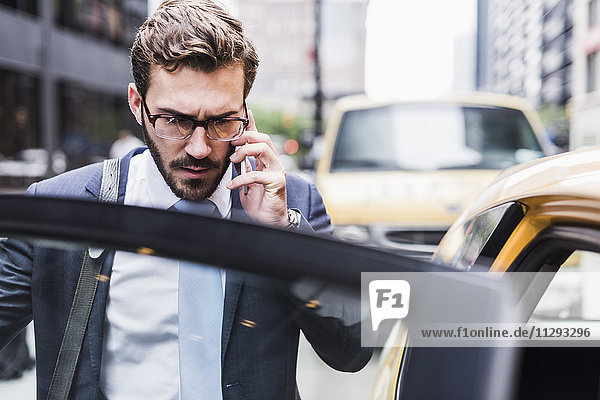 USA  New York City  Geschäftsmann in Manhattan am Handy beim Einsteigen in ein Taxi