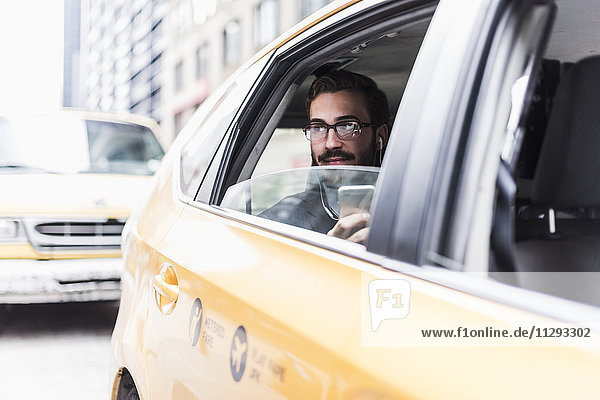 USA  New York City  Geschäftsmann mit Handy und Kopfhörer im Taxi
