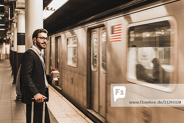 Junger Geschäftsmann wartet am Bahnsteig der U-Bahn-Station und hält Einwegbecher