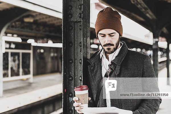 Young man waiting at metro station platform  reading documents
