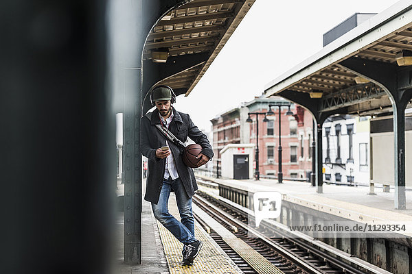 Junger Mann wartet auf die U-Bahn am Bahnsteig  mit Smartphone