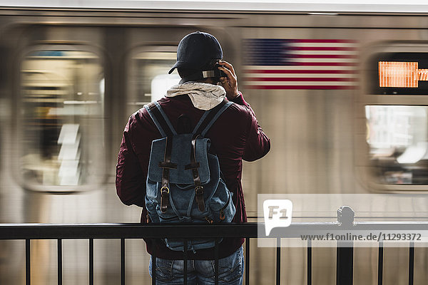 Junger Mann wartet am Bahnsteig auf die U-Bahn und trägt Kopfhörer.