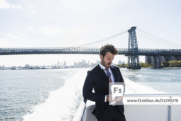 USA  New York City  businessman on ferry on East River checking cell phone