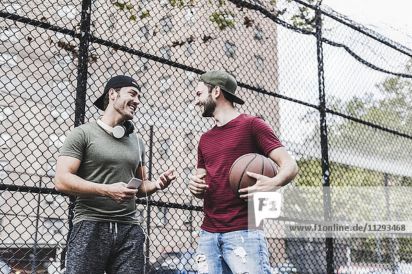 Two smiling friends with basketball outdoors