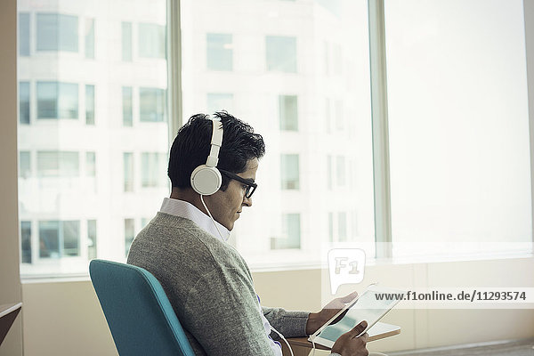 Geschäftsmann im Stuhl sitzend  Kopfhörer tragend  mit digitalem Tablett