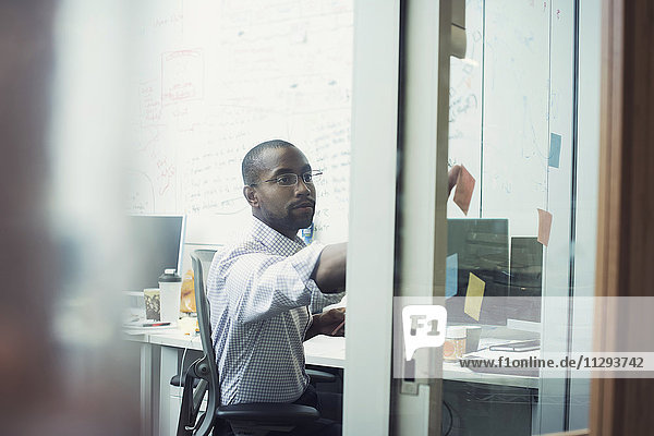 White collar worker sitting in office  sticking notes on glass walll