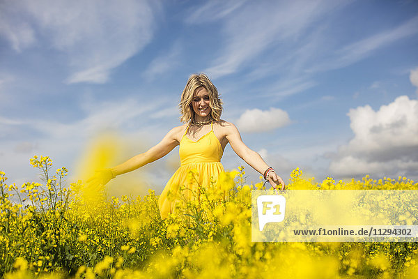Glückliche blonde Frau im gelben Kleid stehend im Rapsfeld