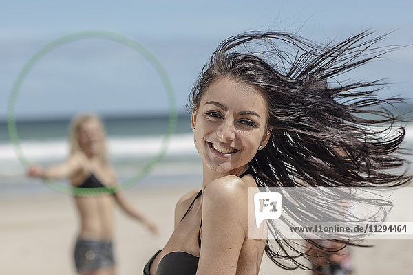 Fröhliche junge Frau am Strand mit Freunden im Hintergrund