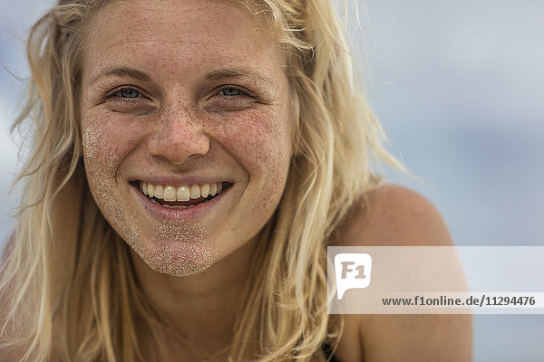 Porträt einer glücklichen jungen Frau mit Sand im Gesicht