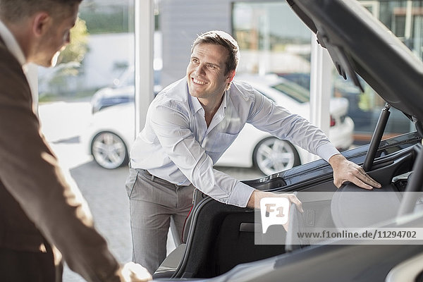 Car dealer opening hatchback of car to customer at car dealership