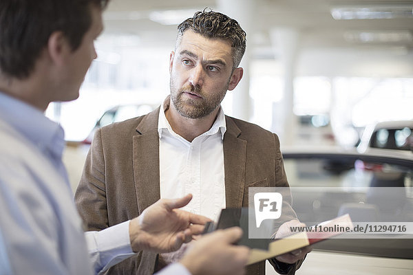 Car dealer handing over color sample to client in showroom