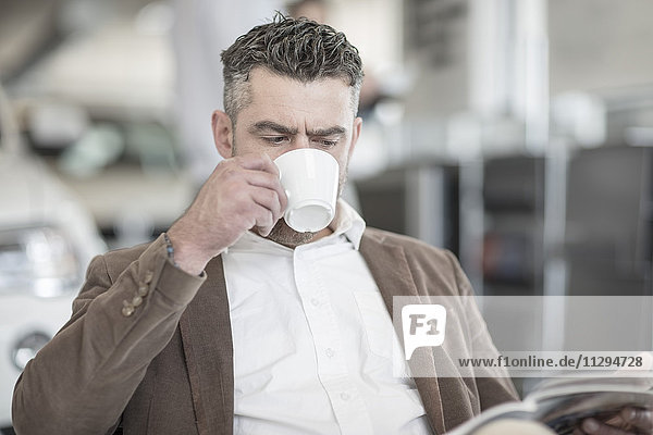 Man drinking coffee reading magazine at car dealership