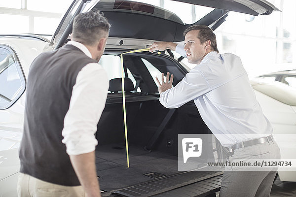 Car dealer opening hatchback of car to customer at car dealership