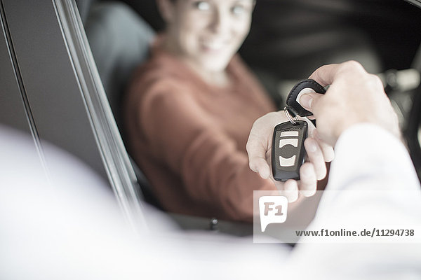 Car dealer handing over key to woman at car dealership