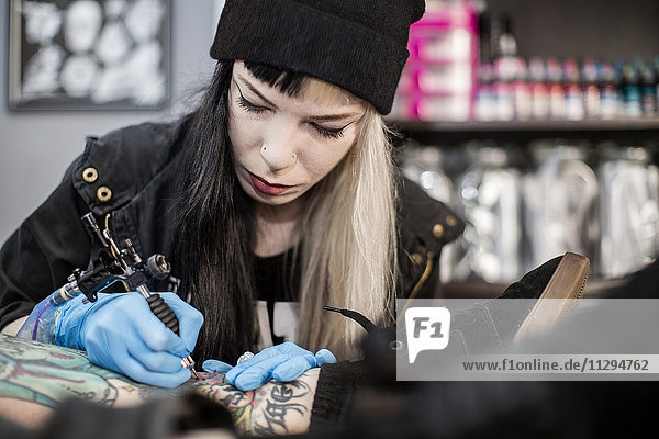 Female tattoo artist tattooing a leg