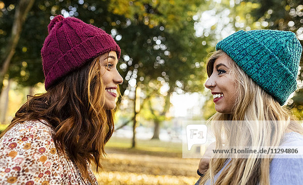 Zwei lächelnde junge Frauen mit Wollmützen in einem Park im Herbst