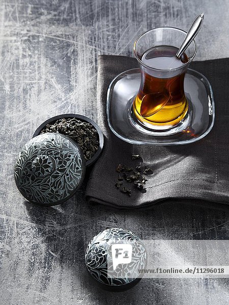 Tee im Glas auf grauer Serviette  Oolong Tee  Heißgetränk  daneben kleine Dose mit Tee gefüllt