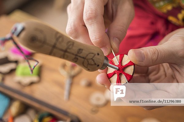 Knopfmacherin  Posamenten Knopf-Rohling aus Holz mit Haltewerkzeug wird mit rotem Garn von Händen umwickelt in Sternmuster und von hinten vernäht  dritter Schritt