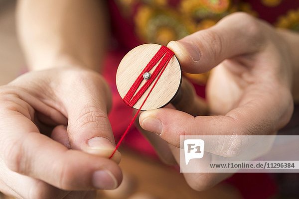 Knopfmacherin  Posamenten Knopf-Rohling aus Holz mit Haltewerkzeug wird mit rotem Garn von Händen umwickelt  zweiter Schritt