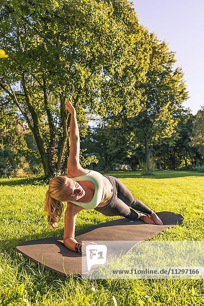 Planks auf der Seite  Junge Frau in Sportkleidung trainiert auf einer Matte in der Wiese in einem Park  München  Oberbayern  Bayern  Deutschland  Europa