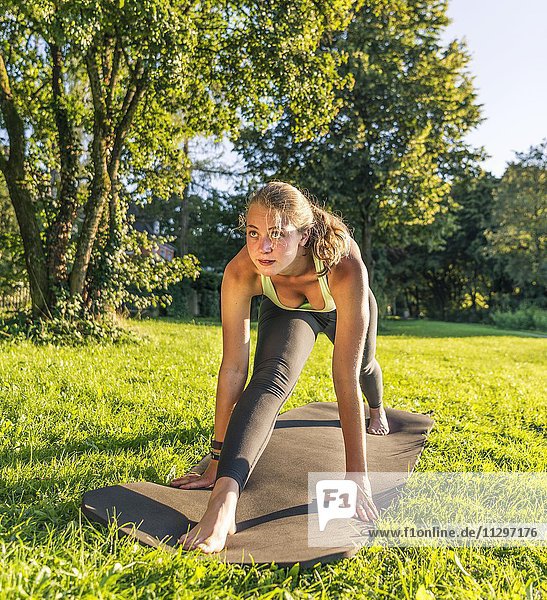 Front Splits  Spagat  Junge Frau in Sportkleidung trainiert auf einer Matte in der Wiese in einem Park  München  Oberbayern  Bayern  Deutschland  Europa
