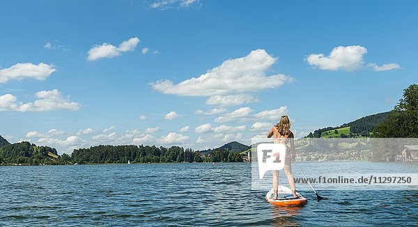 Junge Frau auf einem Stehpaddel Board  Stand-Up-Paddel oder SUP auf einem See  Schliersee  Oberbayern  Bayern  Deutschland  Europa