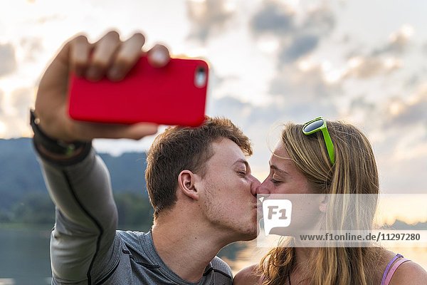 Junges Paar küsst sich  fotografiert sich mit einem Handy selbst  Selfie  Schliersee  Oberbayern  Bayern  Deutschland  Europa