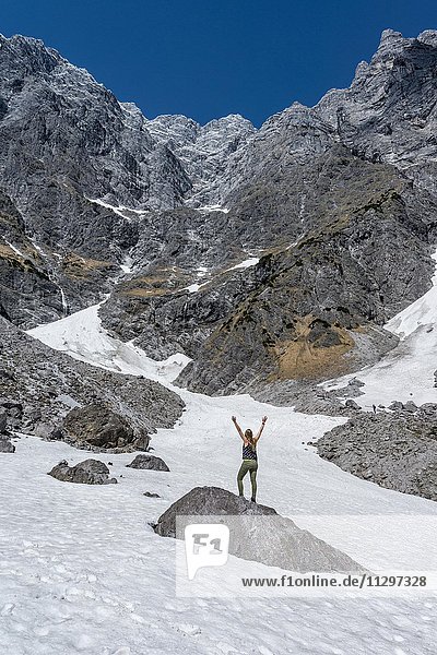 Wanderin steht auf Stein mit ausgestreckten Armen  tiefstes Schneefeld der Deutschen Alpen  Watzmann Ostwand  Berchtesgaden  Bayern  Deutschland  Europa