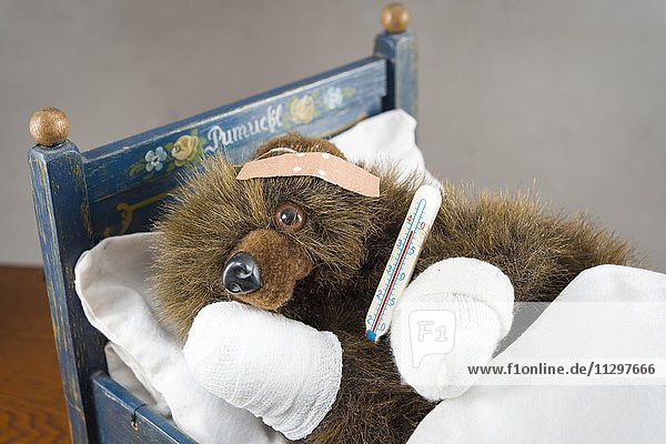 Kranker Teddybär  Pfoten verbunden  Pflaster auf Kopf  Fieberthermometer  liegt in Original Pumuckl Bettchen