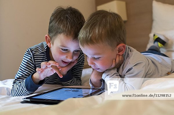Two boys  siblings lying on a bed and playing with an iPad  Tablet PC