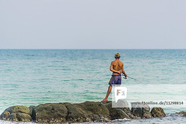 Anglers  local standing on rock in turquoise sea  fishing  Koh Rong  Sihanoukville  Krong Preah Sihanouk  Cambodia  Asia