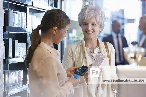 Frau kauft Parfüm im Laden mit kabellosem Kreditkartenleser