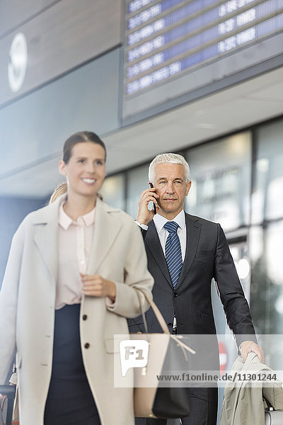 Geschäftsleute beim Gehen und Telefonieren in der Flughafenhalle