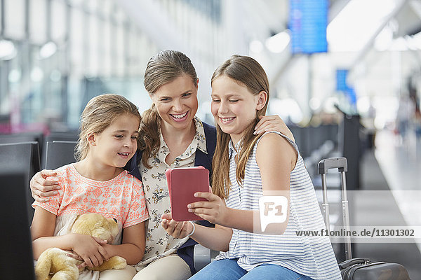 Mutter und Töchter mit digitalem Tablett im Abflugbereich des Flughafens