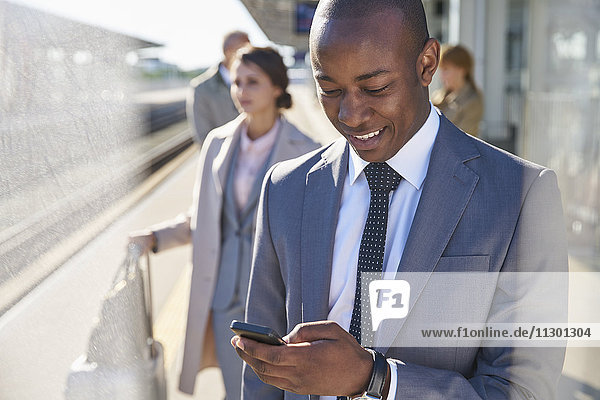 Geschäftsmann SMS mit Handy auf Bahnsteig