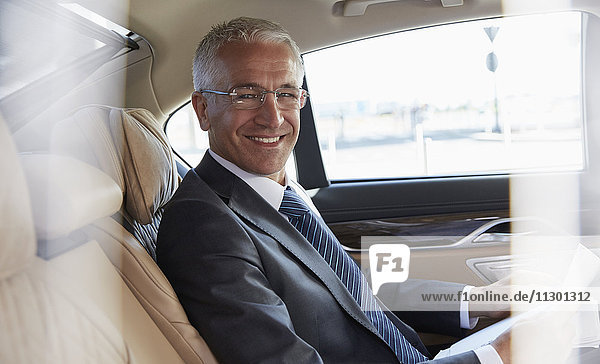 Portrait lächelnder Geschäftsmann auf dem Rücksitz des Stadtautos