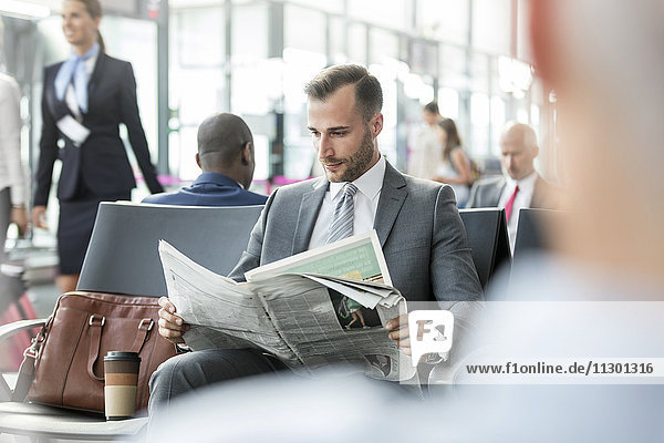 Geschäftsmann liest Zeitung im Abflugbereich des Flughafens