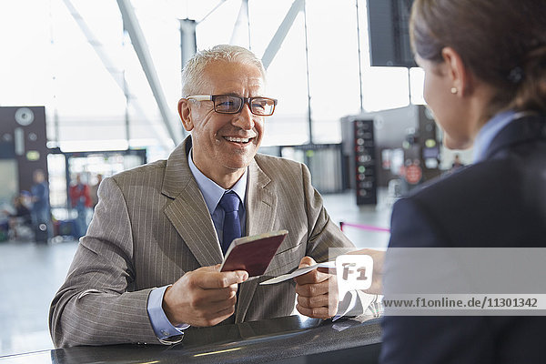Lächelnder Geschäftsmann überreicht dem Kundenbetreuer am Check-in-Schalter des Flughafens einen Pass.
