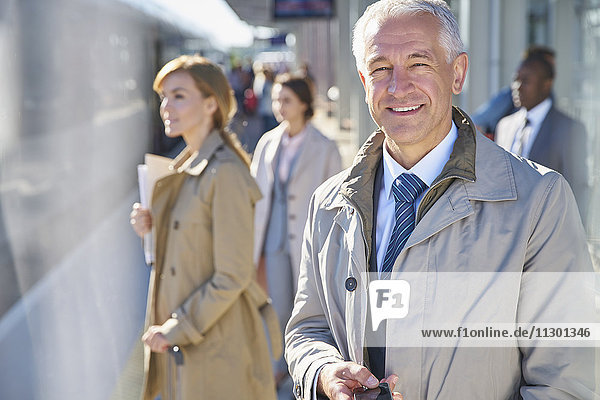 Porträt eines lächelnden Geschäftsmannes auf dem sonnigen Bahnsteig des Bahnhofs