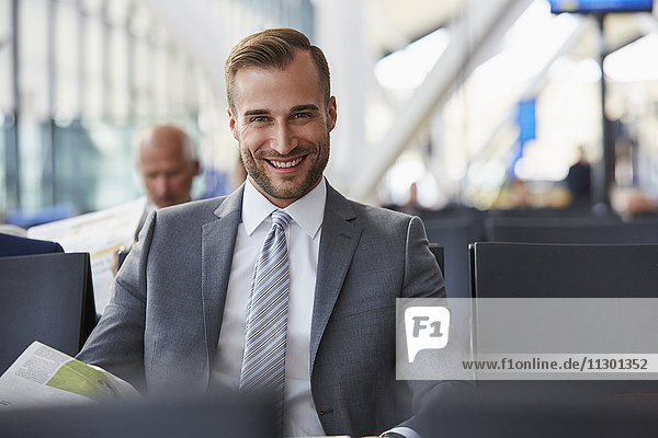 Portrait lächelnder Geschäftsmann beim Zeitungslesen im Abflugbereich des Flughafens