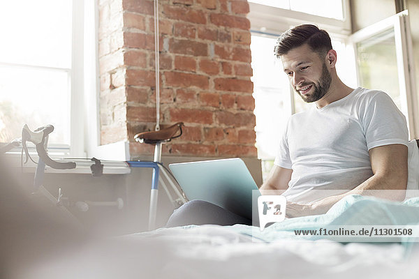 Mann mit Laptop im Bett in der Wohnung