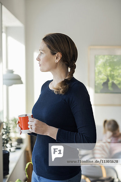 Frau stehend mit Kaffeetasse im Wohnzimmer zu Hause