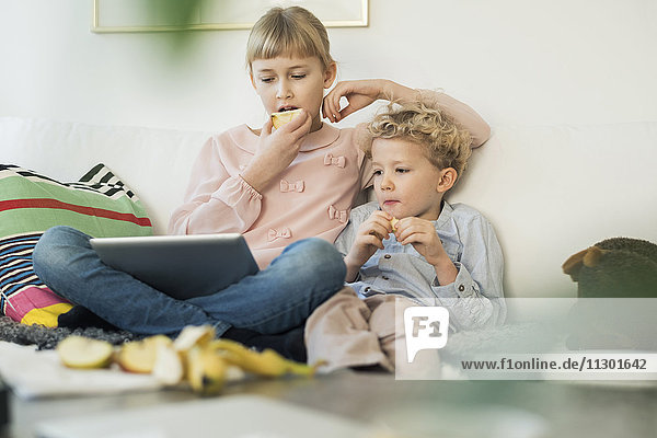 Geschwister  die digitale Tabletten verwenden  während sie zu Hause Äpfel essen.
