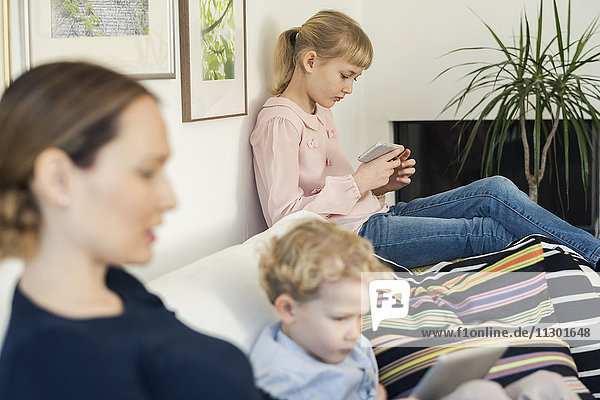 Mother and kids using technologies on sofa at home