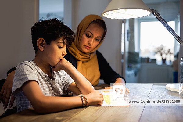 Mutter und Sohn lesen Buch unter der beleuchteten Schreibtischlampe zu Hause
